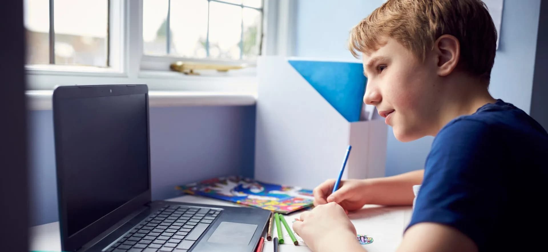 Middle school student writing in a notebook beside a laptop