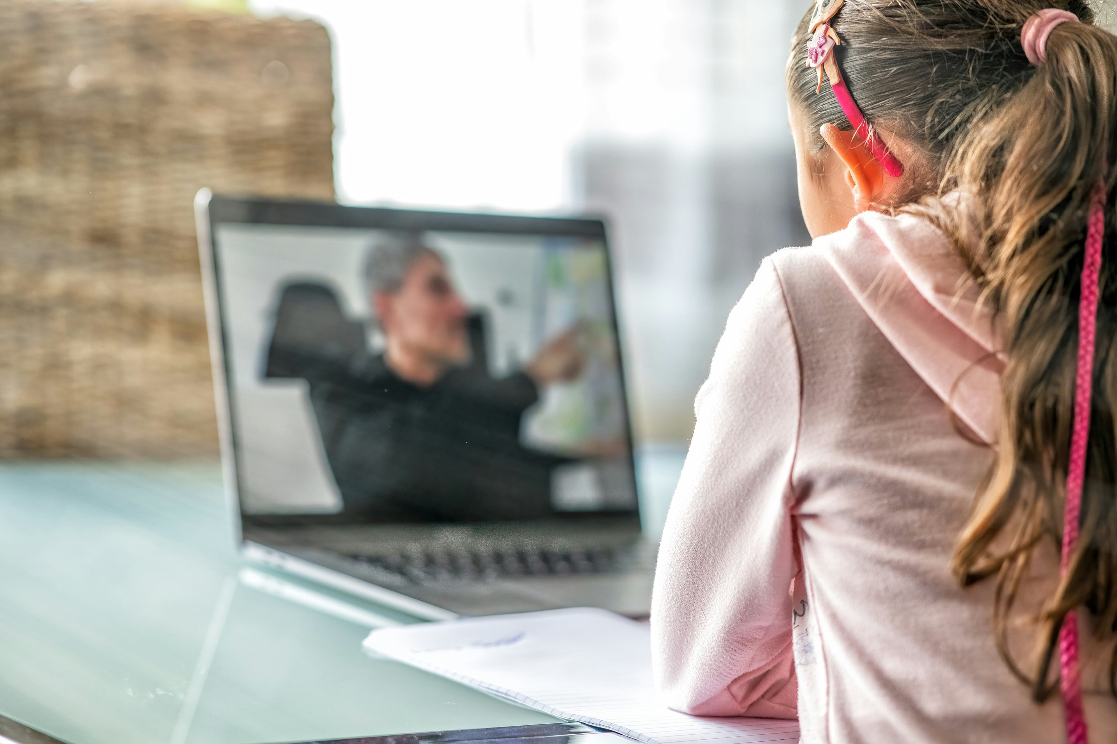 Child watching an adult male on a laptop screen during remote learning.