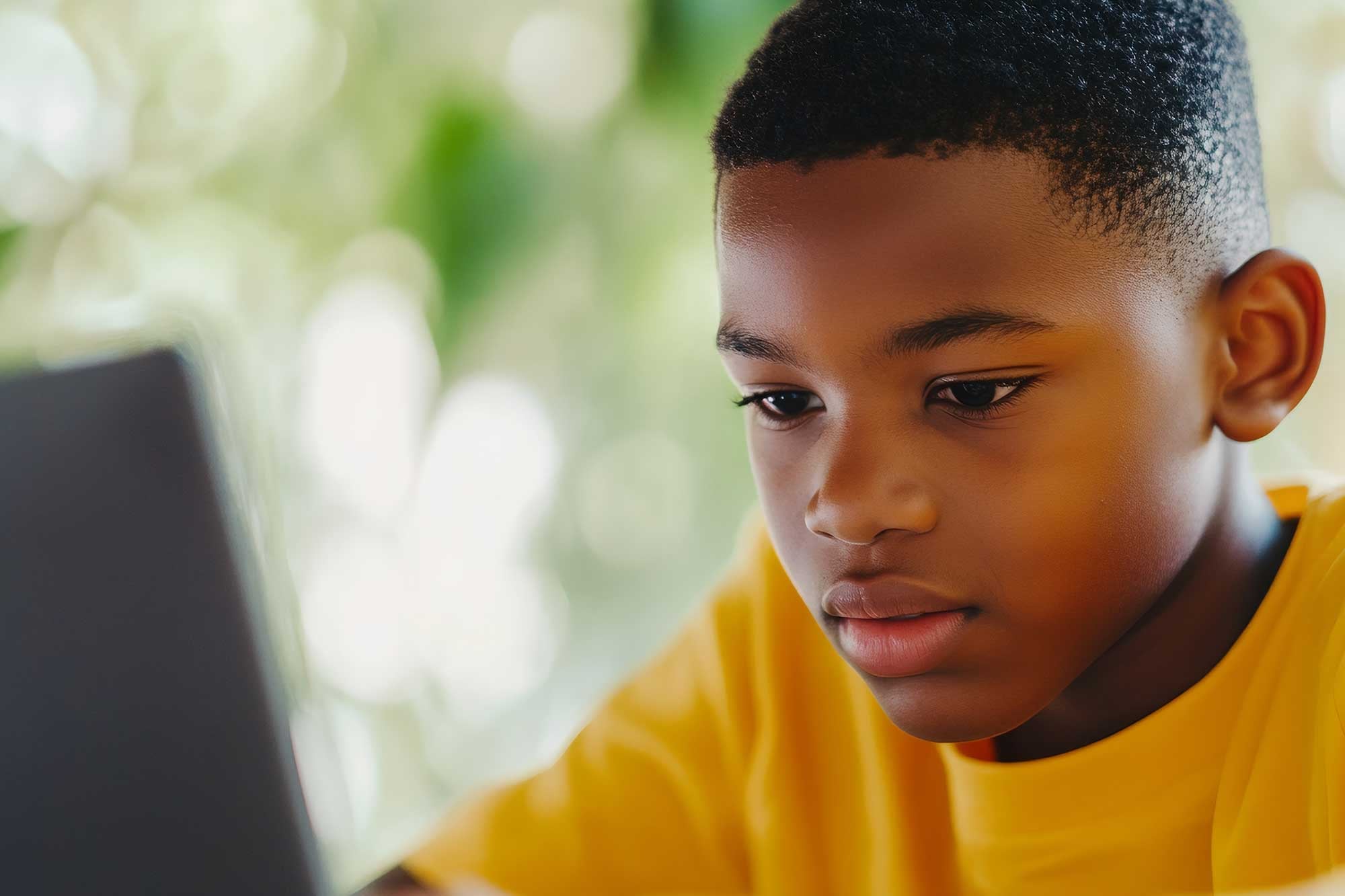 Child in yellow shirt focused on a laptop screen.