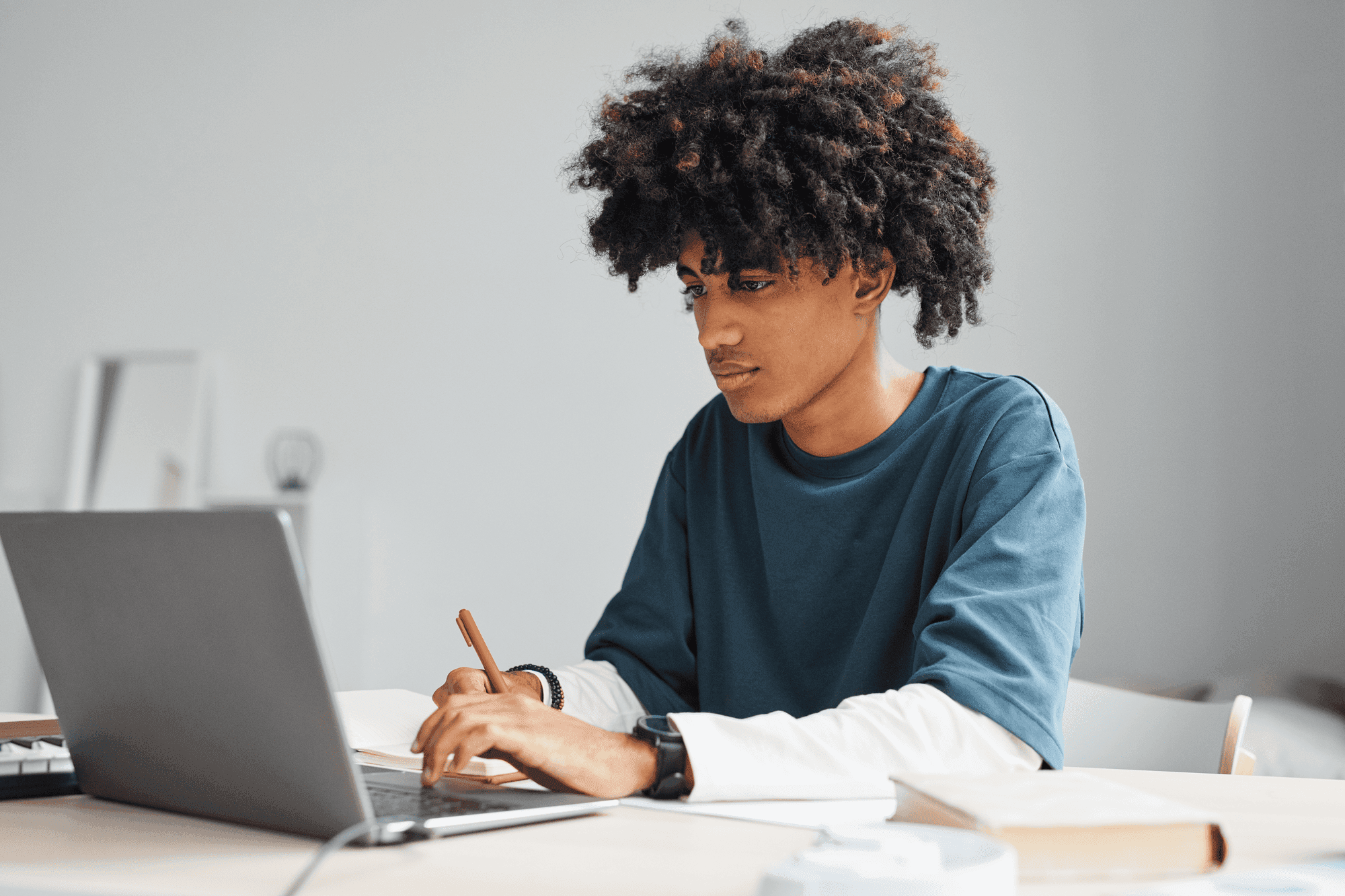 Young adult student working on laptop and writing in a notebook.